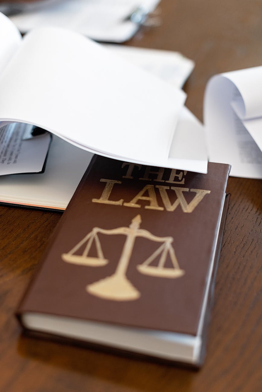 a law book on a wooden desk beside papers, Law Office Education