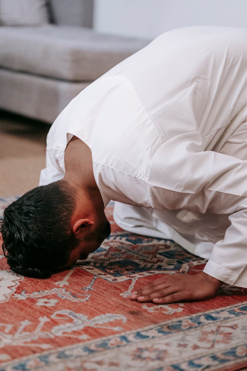 man in white thobe bowing down on red and blue rug