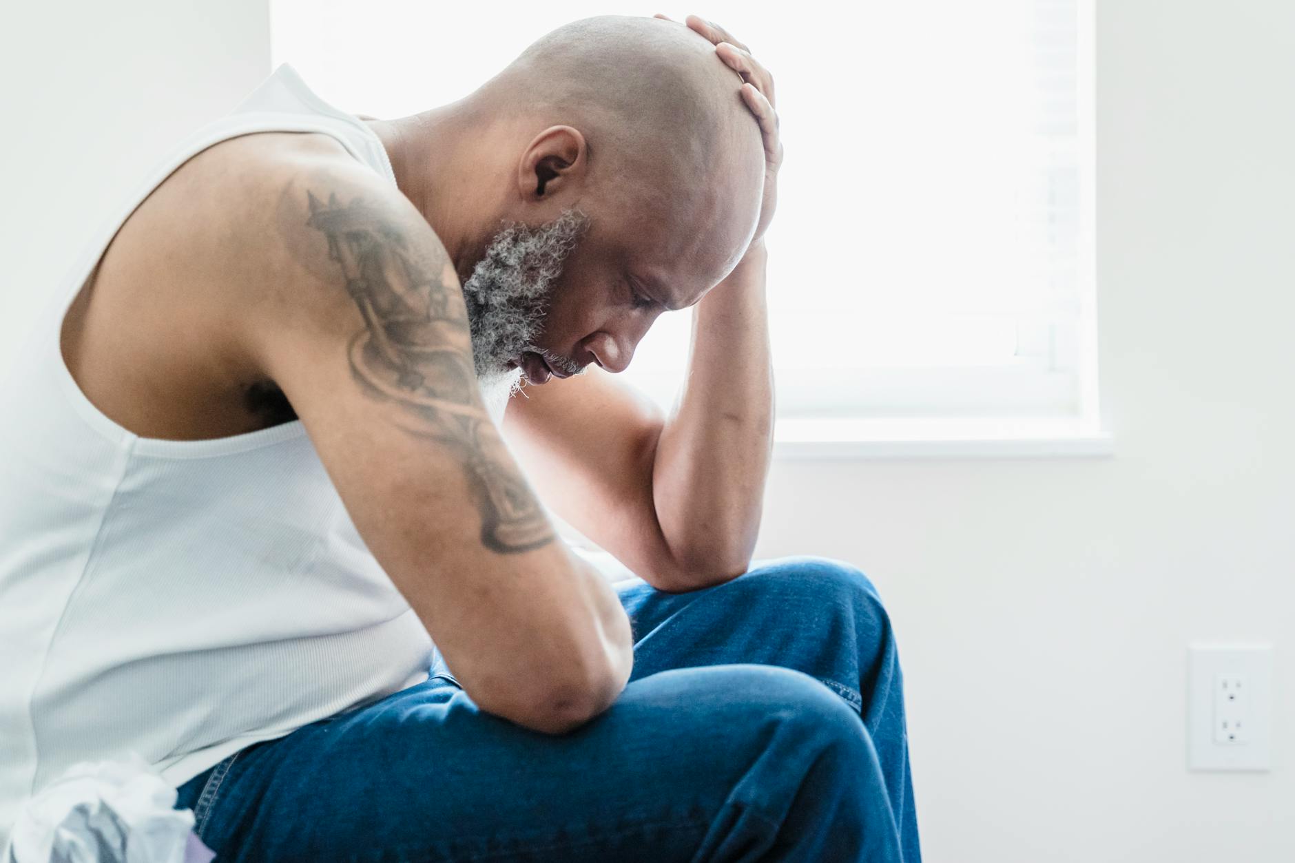 man in white tank top and blue denim jeans sitting