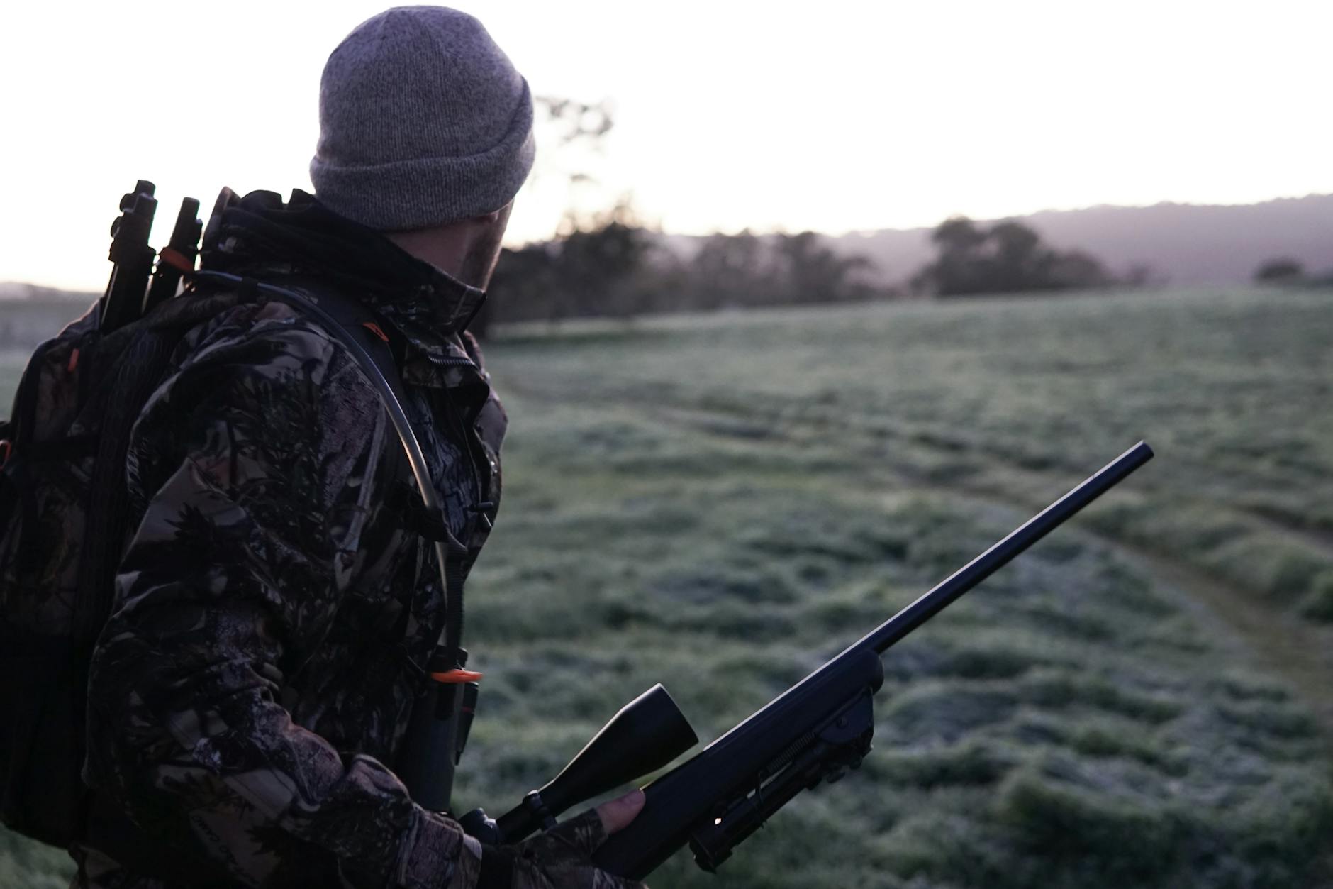 man wearing gray and black camouflage jacket holding rifle walking on grass field